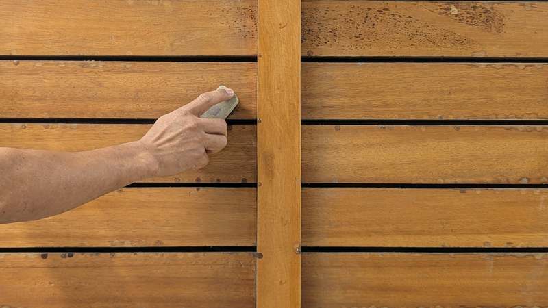 Close-up of a professional-grade belt sander smoothing wood grain on a pine workbench, with sanding dust visible, in a well-lit garage workshop